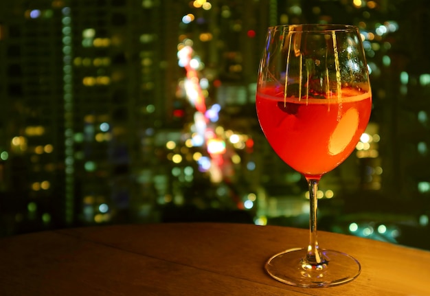 Bicchiere di cocktail rosso vivo isolato sul tavolo delle terrazze sul tetto con vista notturna urbana sfocata
