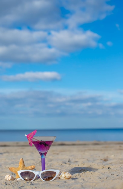 Bicchiere di cocktail sulla spiaggia sabbiosa e occhiali da sole vicino al mare. Vacanze estive, concetto di vacanza.
