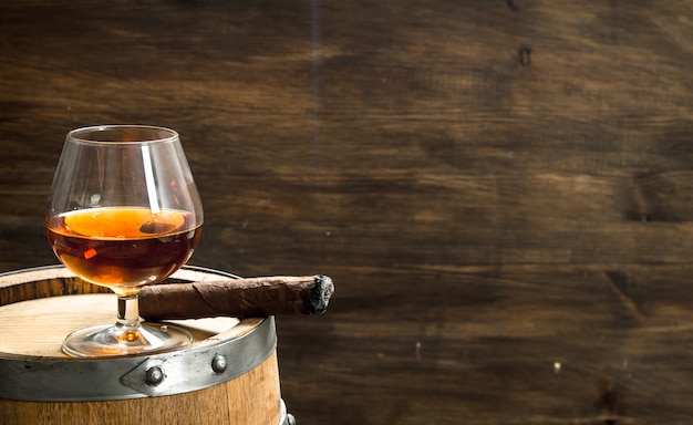 Bicchiere di cognac con un sigaro su un barile. Su uno sfondo di legno.