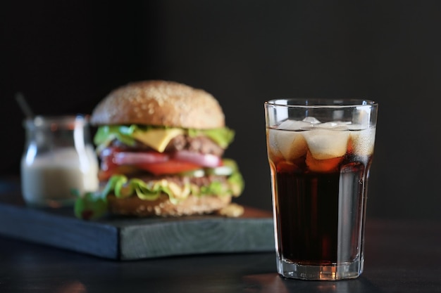 Bicchiere di cola fredda con gustoso hamburger su sfondo scuro