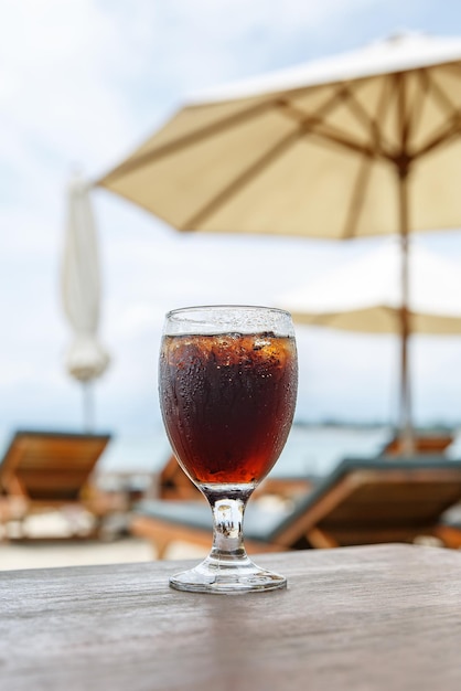 Bicchiere di cola sulla spiaggia con ombrelloni Bevanda rinfrescante