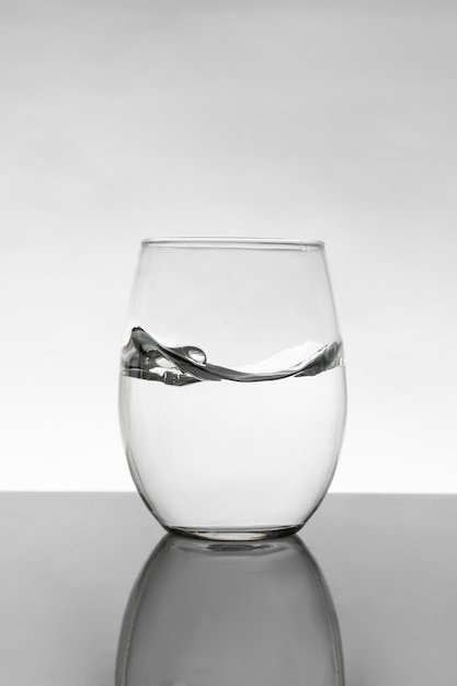 Bicchiere di cristallo con acqua in movimento e sfondo bianco con sfumatura grigia