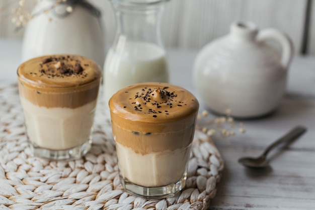 Bicchiere di Iced Dalgona Coffee, un caffè alla moda e cremoso panna montata e latte su legno bianco.