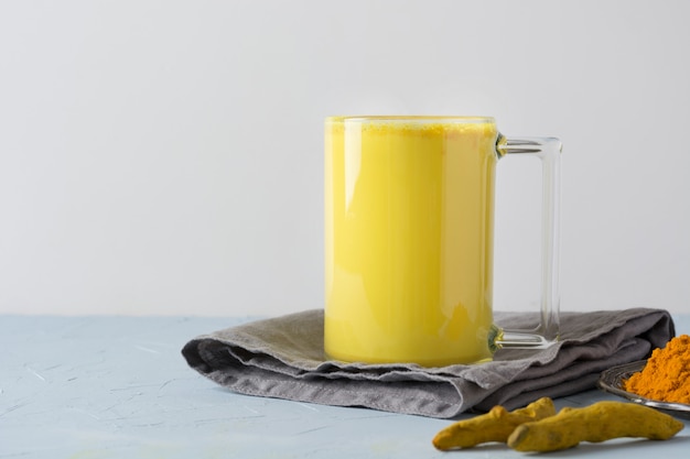 Bicchiere di latte ayurvedico dorato di latte di curcuma con polvere di curcuma su bianco.