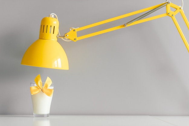 Bicchiere di latte con la cravatta a farfalla gialla che sta sulla tavola sotto la lampada.