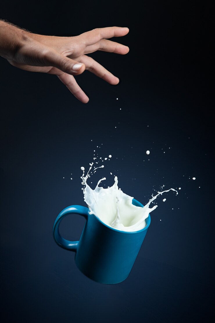Bicchiere di latte con schizzi che cadono dalla mano su sfondo blu scuro.