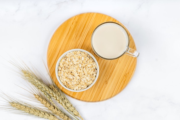 Bicchiere di latte d'avena con fiocchi d'avena su fondo di legno bianco