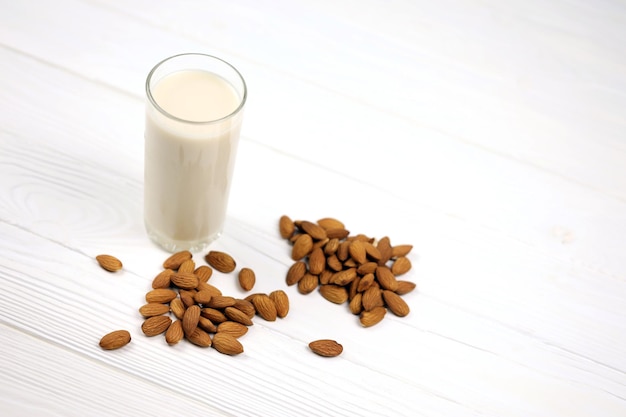 Bicchiere di latte di mandorla con noci di mandorle su tavola di legno bianca Latte alternativo ai latticini per una dieta sana e disintossicante