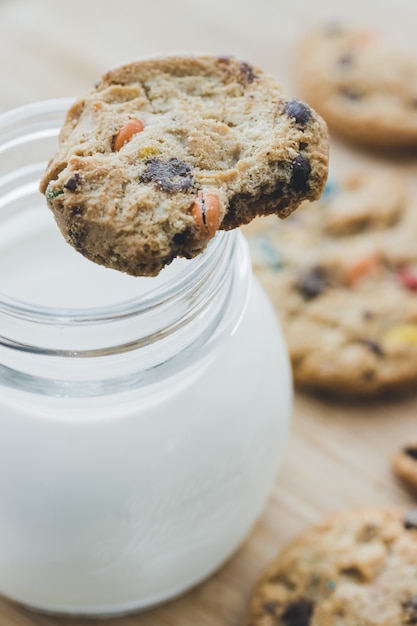 Bicchiere di latte e biscotti con le caramelle di cioccolato variopinte su un bordo di legno