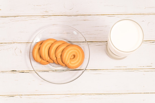 Bicchiere di latte e biscotti in una ciotola di vetro su fondo di legno bianco