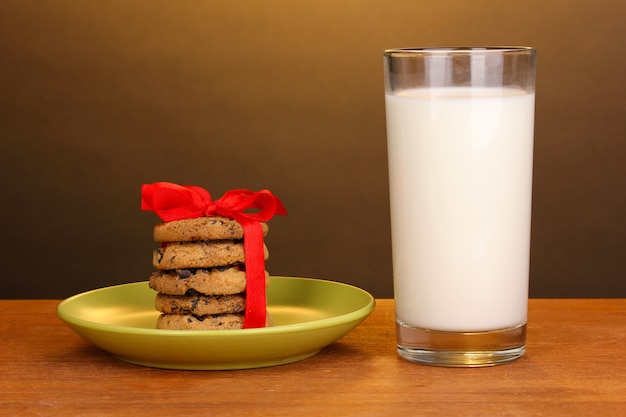 Bicchiere di latte e biscotti sul tavolo di legno su superficie marrone