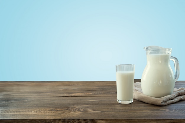 Bicchiere di latte e brocca freschi sul ripiano del tavolo in legno con parete blu come sfondo.