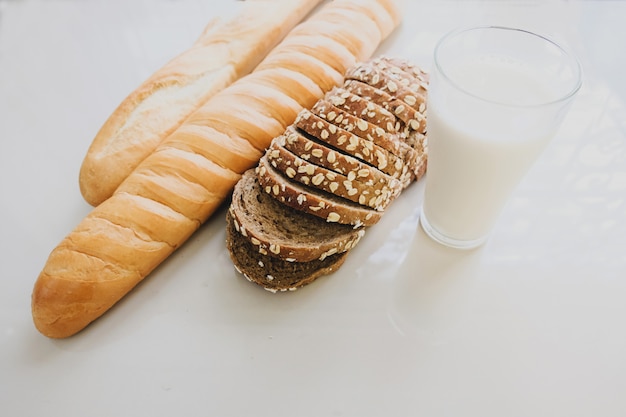 Bicchiere di latte e pane posto su un tavolo bianco.