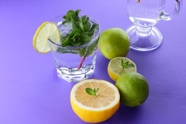 Bicchiere di mojito con ghiaccio e menta Primo piano di cocktail con diversi tipi di agrumi su sfondo viola