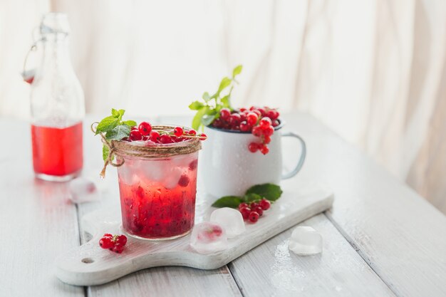 Bicchiere di ribes rosso cocktail o mocktail, rinfrescante bevanda estiva con ghiaccio tritato e acqua frizzante su una superficie di legno bianca