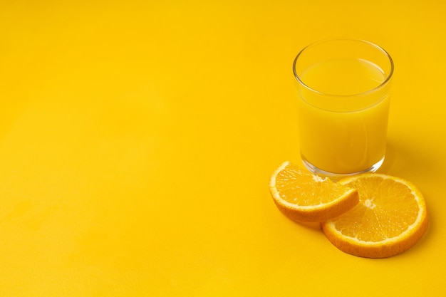Bicchiere di succo d'arancia appena spremuto con frutta su sfondo giallo