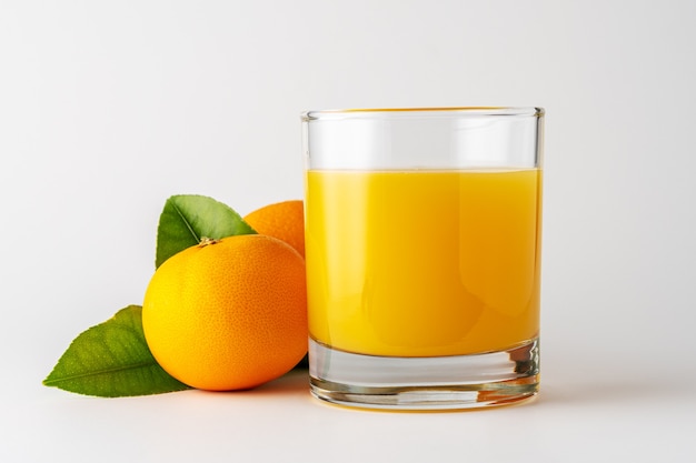Bicchiere di succo d'arancia e frutta arancione su sfondo bianco.
