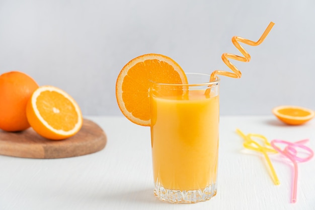 Bicchiere di succo d'arancia fresco servito con fetta di agrumi e paglia su fondo di legno bianco