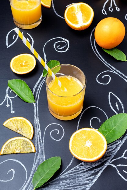 Bicchiere di succo d'arancia su sfondo scuro con rami dipinti, foglie di arancio reali e fette di frutta.