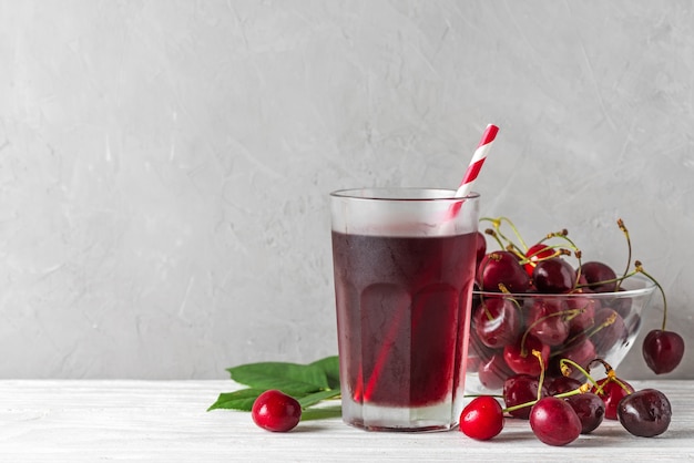 Bicchiere di succo di ciliegia freddo con una cannuccia e bacche fresche su bianco. Bevanda estiva di ristoro