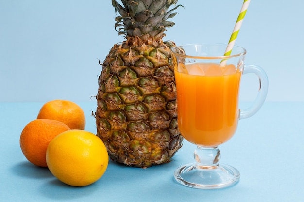 Bicchiere di succo di frutta, ananas fresco, limone e mandarino su sfondo blu.