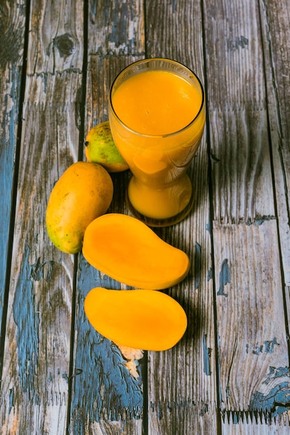 Bicchiere di succo di mango e mango affettato sul tavolo di legno. Scena colorata.