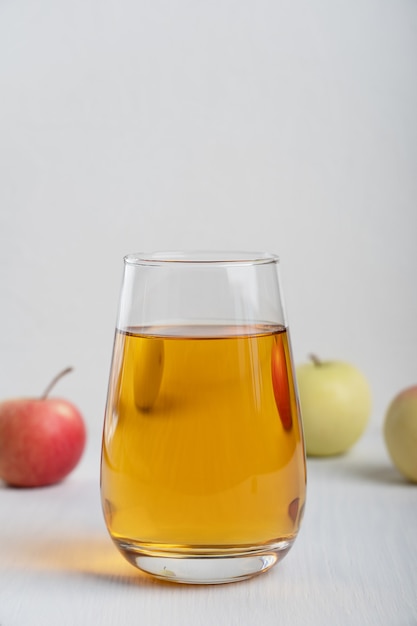 Bicchiere di succo di mela in piedi sul tavolo di legno bianco circondato da frutta cruda