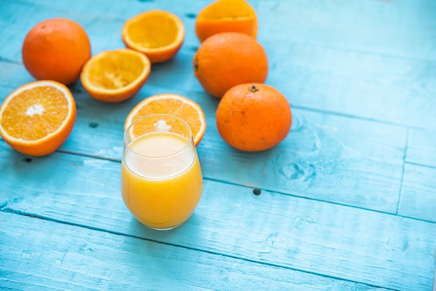 Bicchiere di succo naturale di diverse arance biologiche, alcune intere, altre spremute, per la dieta, su un tavolo di legno blu. Colazione salutare