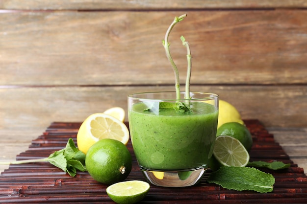 Bicchiere di succo verde sano con menta e frutta su fondo in legno