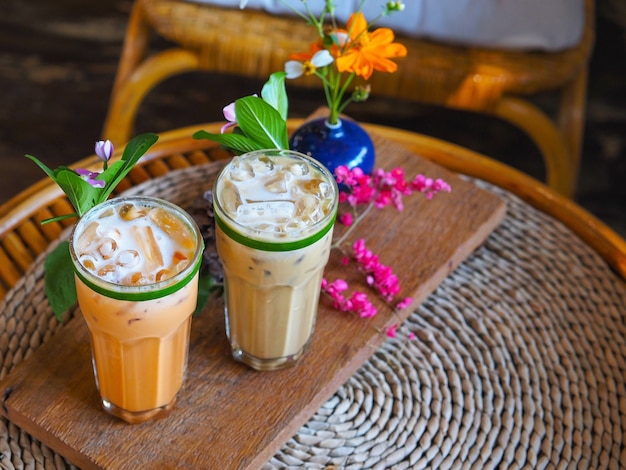 bicchiere di tè al latte tailandese e caffè freddo con decorazioni floreali su tavolo vintage in legno al bar.