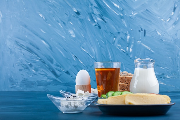 Bicchiere di tè, latte e piatto di burro sul tavolo blu.