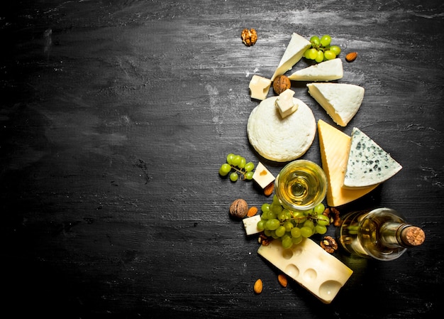 Bicchiere di vino bianco con diversi formaggi, uva e noci. Sul tavolo di legno nero.