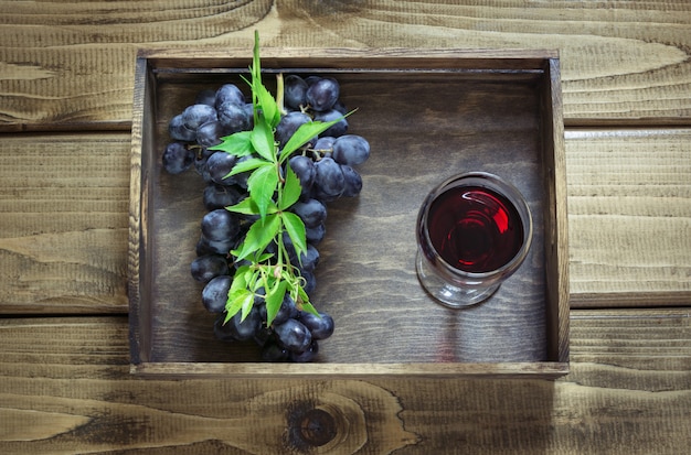Bicchiere di vino con vino rosso e uva matura sul bordo di legno.