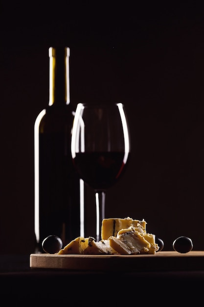Bicchiere di vino e bottiglia, formaggio con muffa e uva su sfondo nero