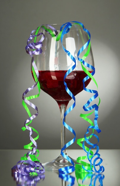 Bicchiere di vino rosso e streamer dopo la festa su sfondo grigio