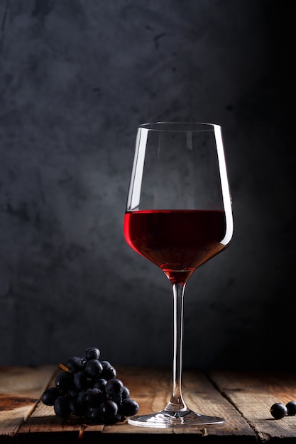 Bicchiere di vino rosso e un grappolo d'uva su un vecchio tavolo di legno.