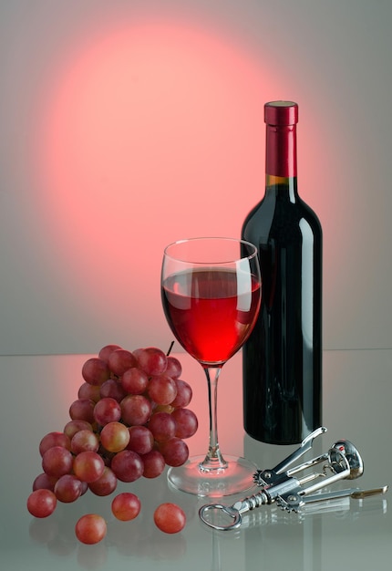 Bicchiere di vino rosso, pennello di uva rossa, bottiglia di vino e cavatappi in metallo su sfondo colorato. Retroilluminazione. Copia-spazio.