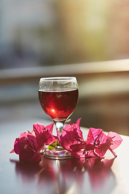 Bicchiere di vino rosso su sfondo sfocato di montagna Decorazioni di fiori di bouganville rosa con luce solare Fotografia dell'ora blu Concetto di cena romantica Spazio di copia