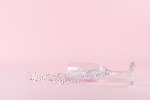 Bicchiere di vino rovesciato con diamanti su sfondo rosa Concetto di festa minimo creativo