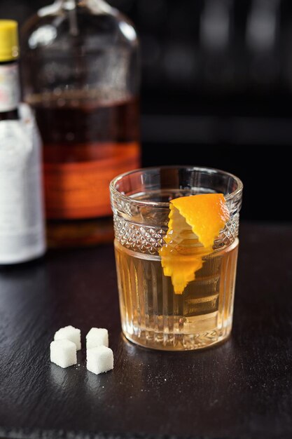 Bicchiere di whisky cognac o brandy con limone e cubetti di ghiaccio in piedi sul bancone del bar con una bottiglia sullo sfondo