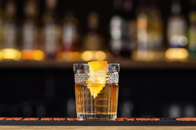 Bicchiere di whisky cognac o brandy con limone e cubetti di ghiaccio in piedi sul bancone del bar