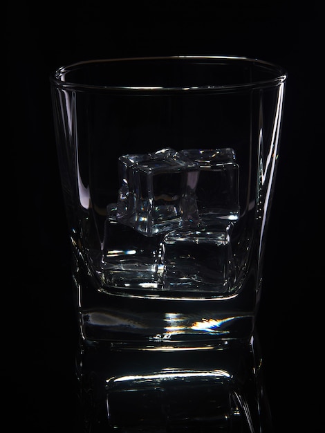 Bicchiere di whisky con ghiaccio su uno sfondo nero con la riflessione