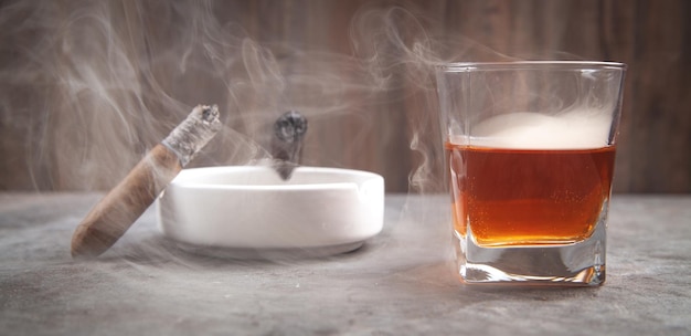 Bicchiere di whisky posacenere e sigari sul tavolo
