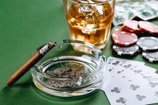 Bicchiere di whisky sigaro carte da gioco e fiches sulla superficie verde
