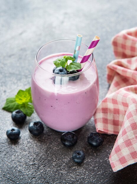 Bicchiere di yogurt ai mirtilli con mirtilli su uno sfondo di pietra grigia.