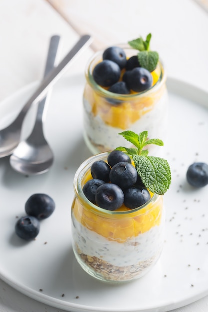 Bicchiere di yogurt con mirtilli e mousse di mango su uno sfondo bianco