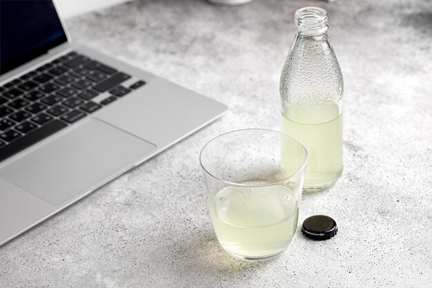 Bicchiere e bottiglia di limonata sul tavolo con un laptop. Minimalismo. Orario di lavoro. Lavoro a distanza