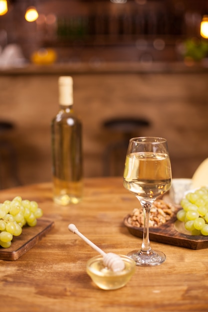 Bicchiere e bottiglia di vino bianco accanto a uva fresca su un tavolo di legno in un pub vintage. Noci marroni. Ciotola di delizioso miele dorato.