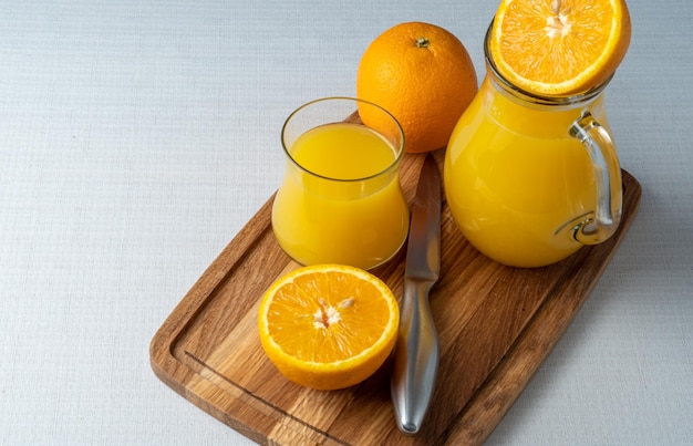 Bicchiere e brocca di succo d'arancia su un supporto di legno affettato sfondo di lino arancione