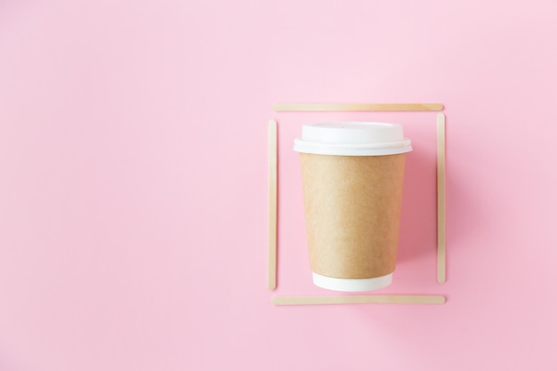 Bicchiere ecologico usa e getta con coperchio in plastica per caffè con cornice di bastoncini di legno su sfondo rosa...